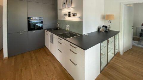 Projekt vom Küchenzentrum Steffl ewe Küche Weiß kombiniert mit Dunkelgrau, Griffküche, Glasrückwand glänzend, Wandbord mit Beleuchtung, Siemens Geräte