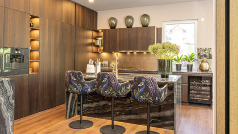 Designküche Marke LEICHT mit Holzfronten Walnuss dunkel, Natursteinarbeitsplatten und Seitenwangen, Kochinsel, Gaggenau Geräte, Glasrückwand, offene Regale